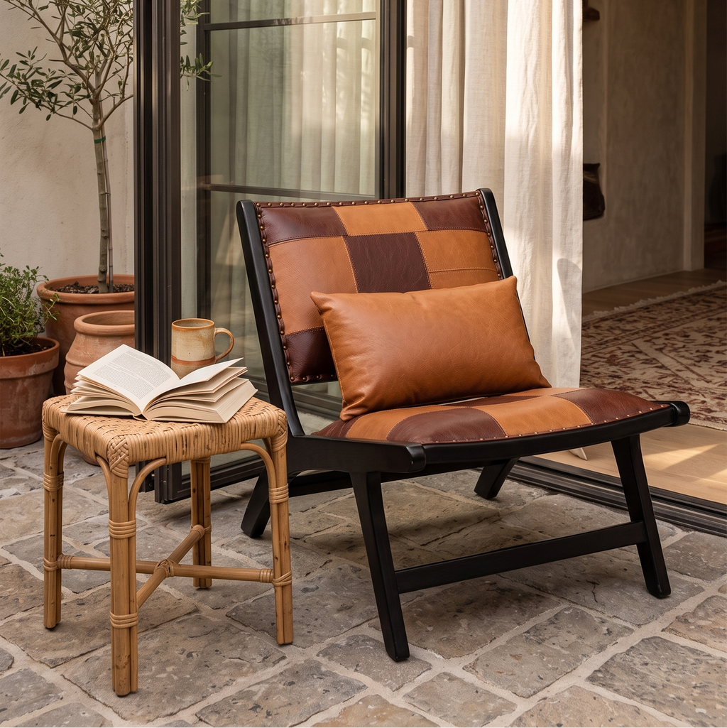 Patchwork leather-look lounge chair on a stone patio beside a rattan stool and potted olive tree
