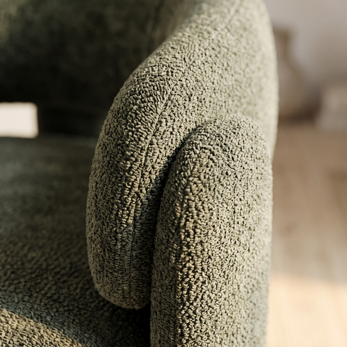 Close-up of olive green boucle texture on the curved arm and rounded back of a barrel accent chair