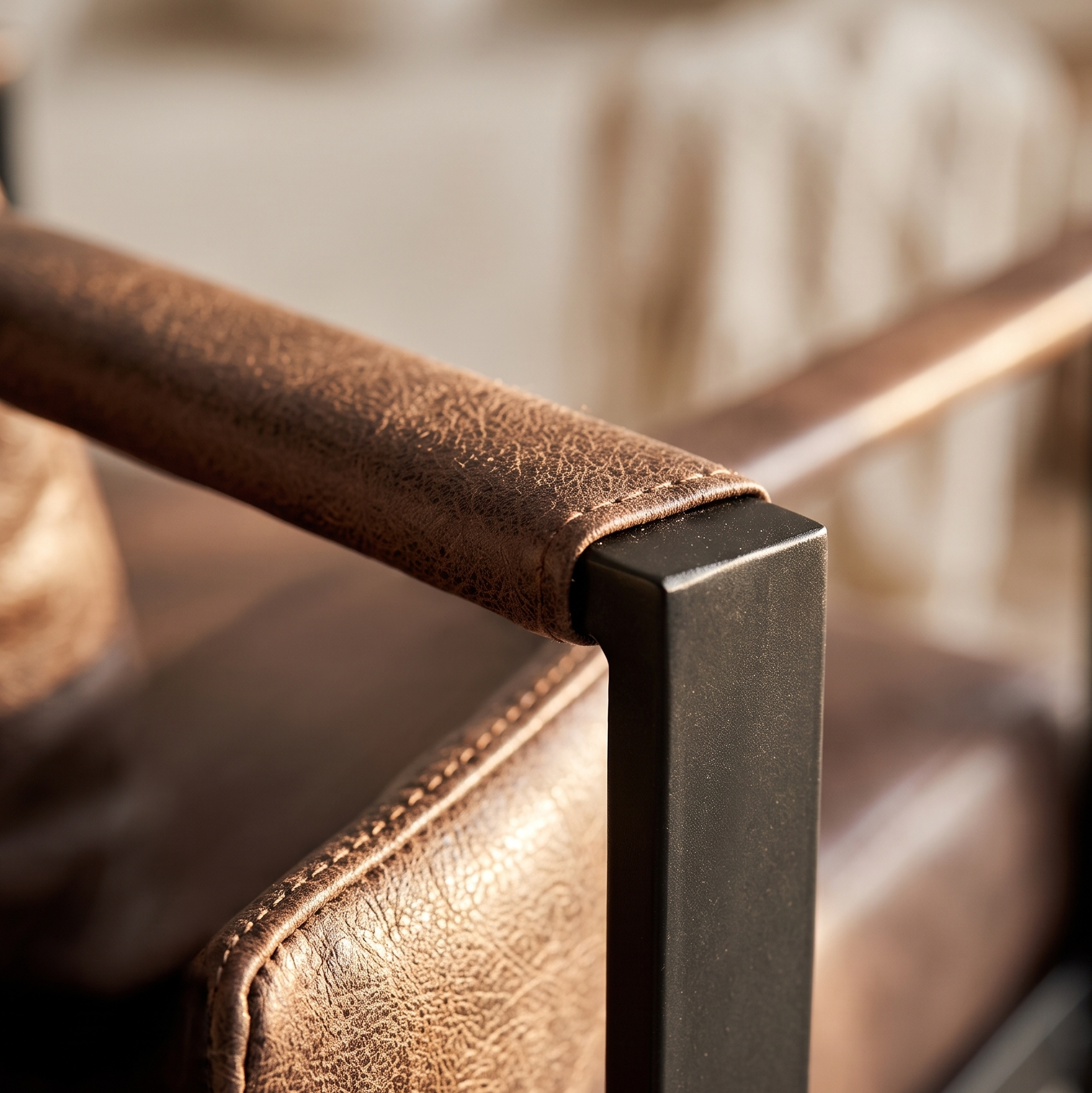 Close-up of stitched brown leather-look armrest meeting the matte black metal frame of an accent chair