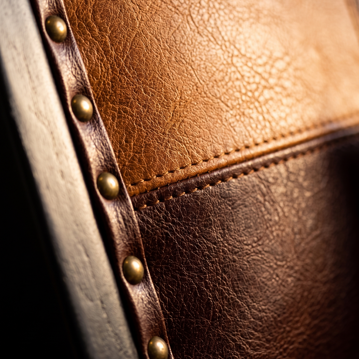 Close-up of cognac and brown patchwork leather-look panels with antique brass nailhead trim