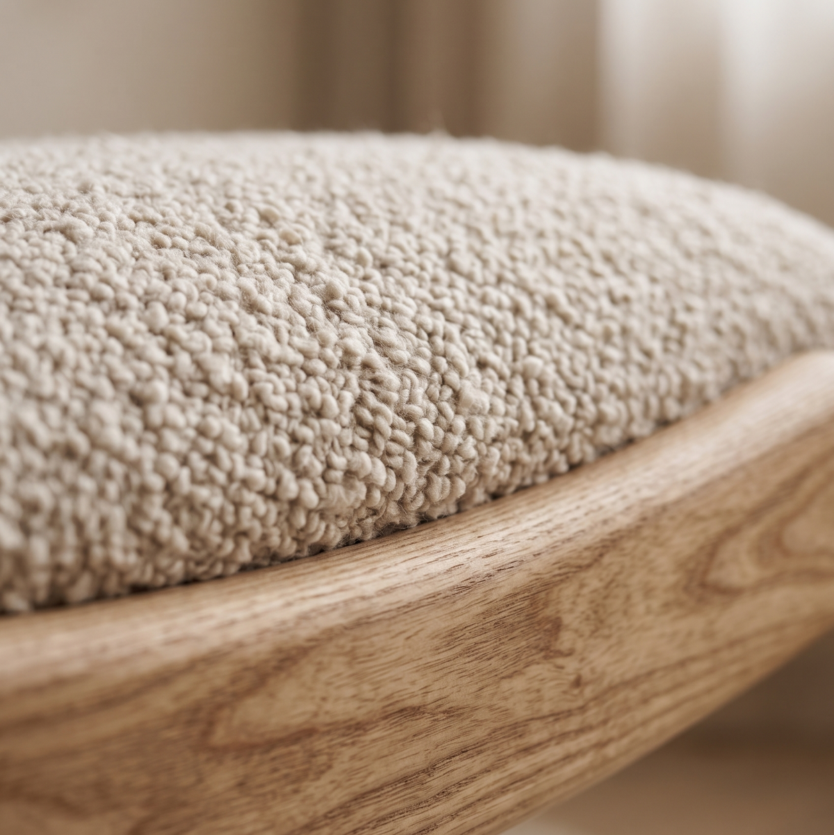 Close-up of cream boucle cushion resting on the curved solid oak base of a floor lounge chair