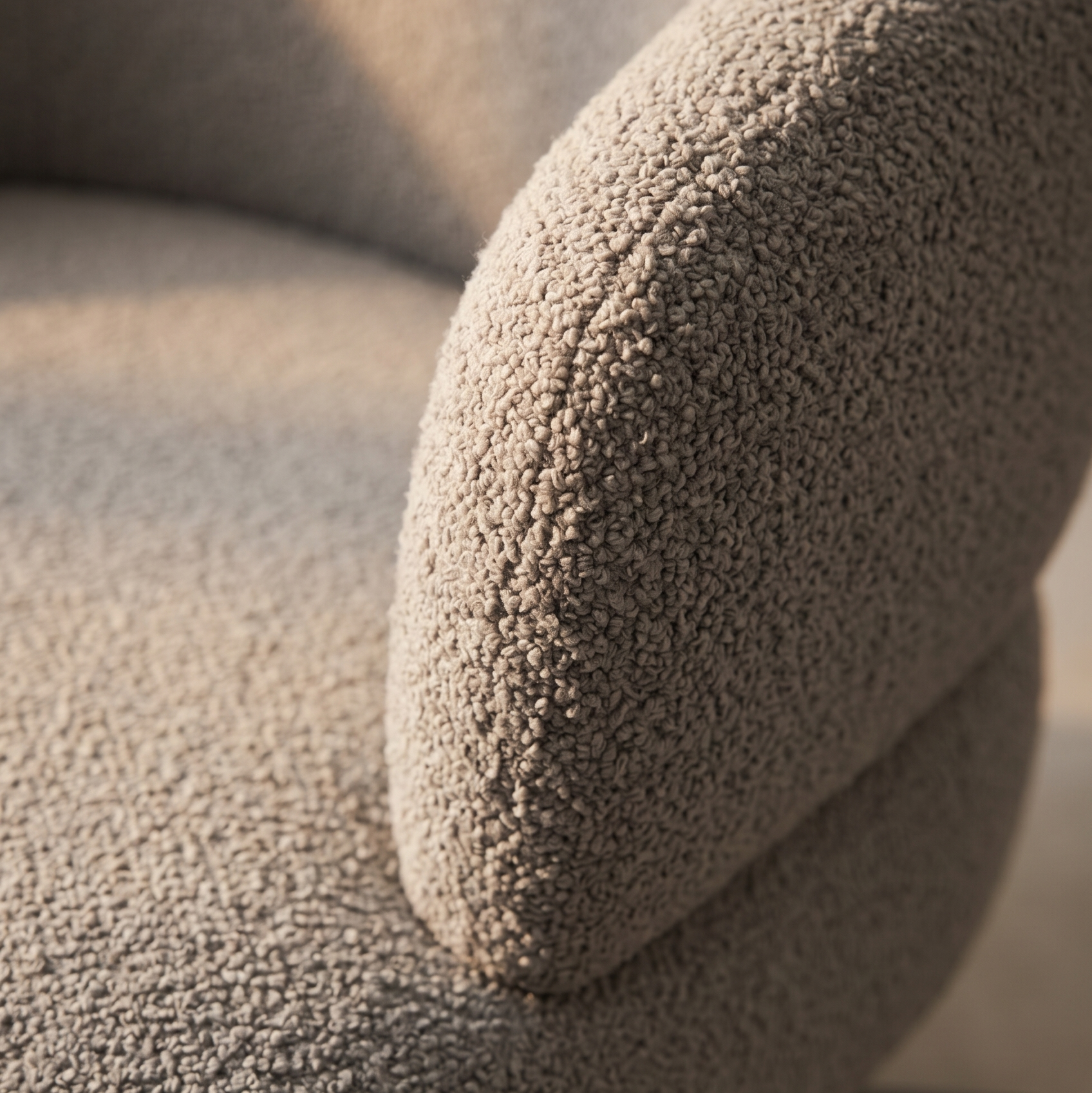 Close-up of textured taupe boucle upholstery on the curved armrest and seat of a swivel chair