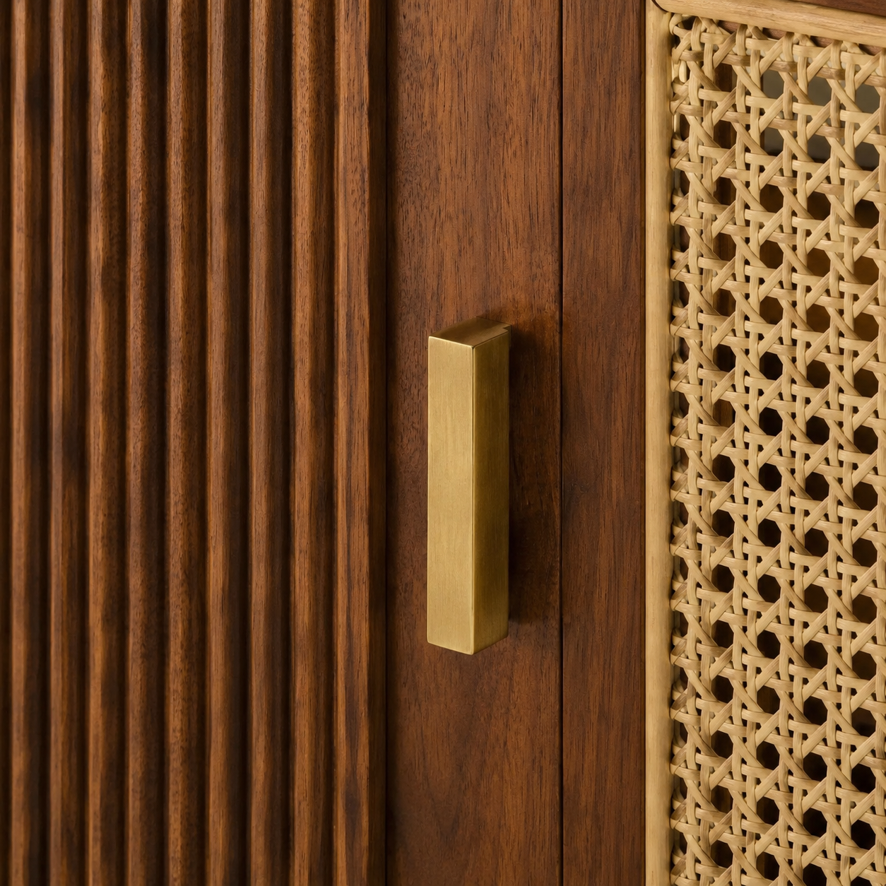 Brushed brass pull between fluted walnut door and natural rattan cane weave close-up